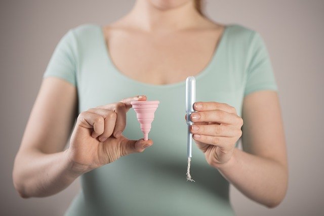Žena drží v rukách tampón a kalíšok.jpg